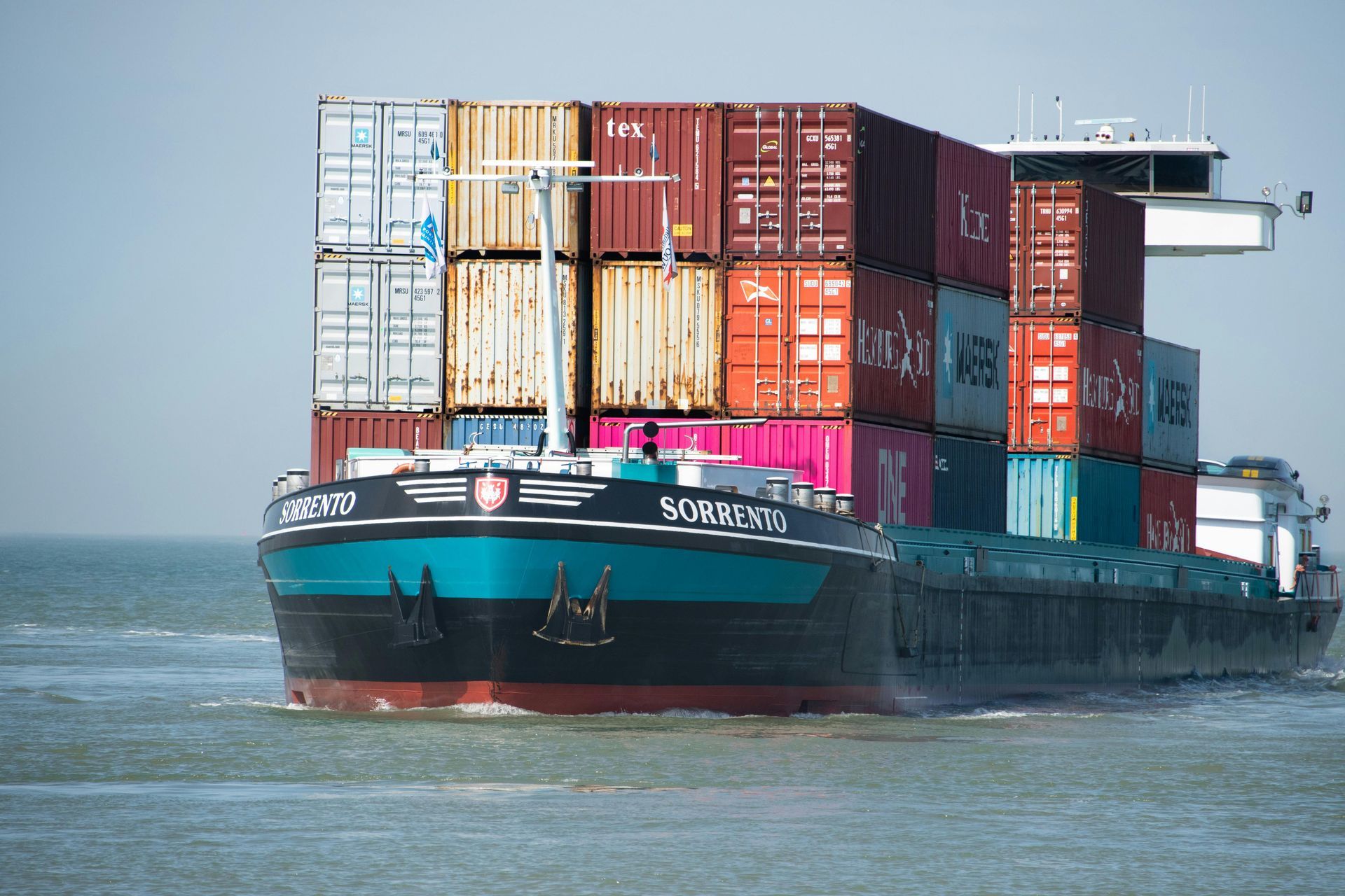 Cargo ship carrying shipping containers at sea. Turquoise hull, blue water.