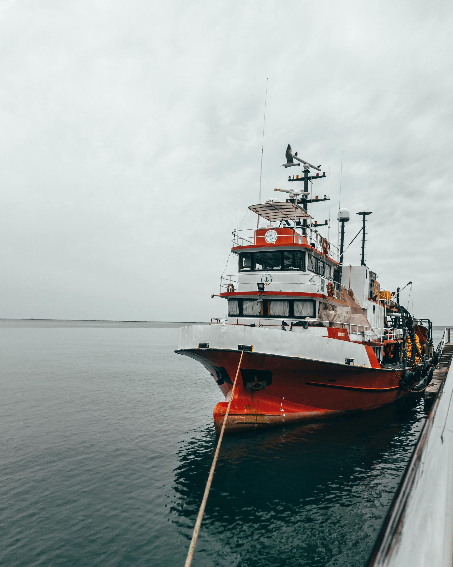 Red and white fishing boat tied to a dock on a cloudy day.