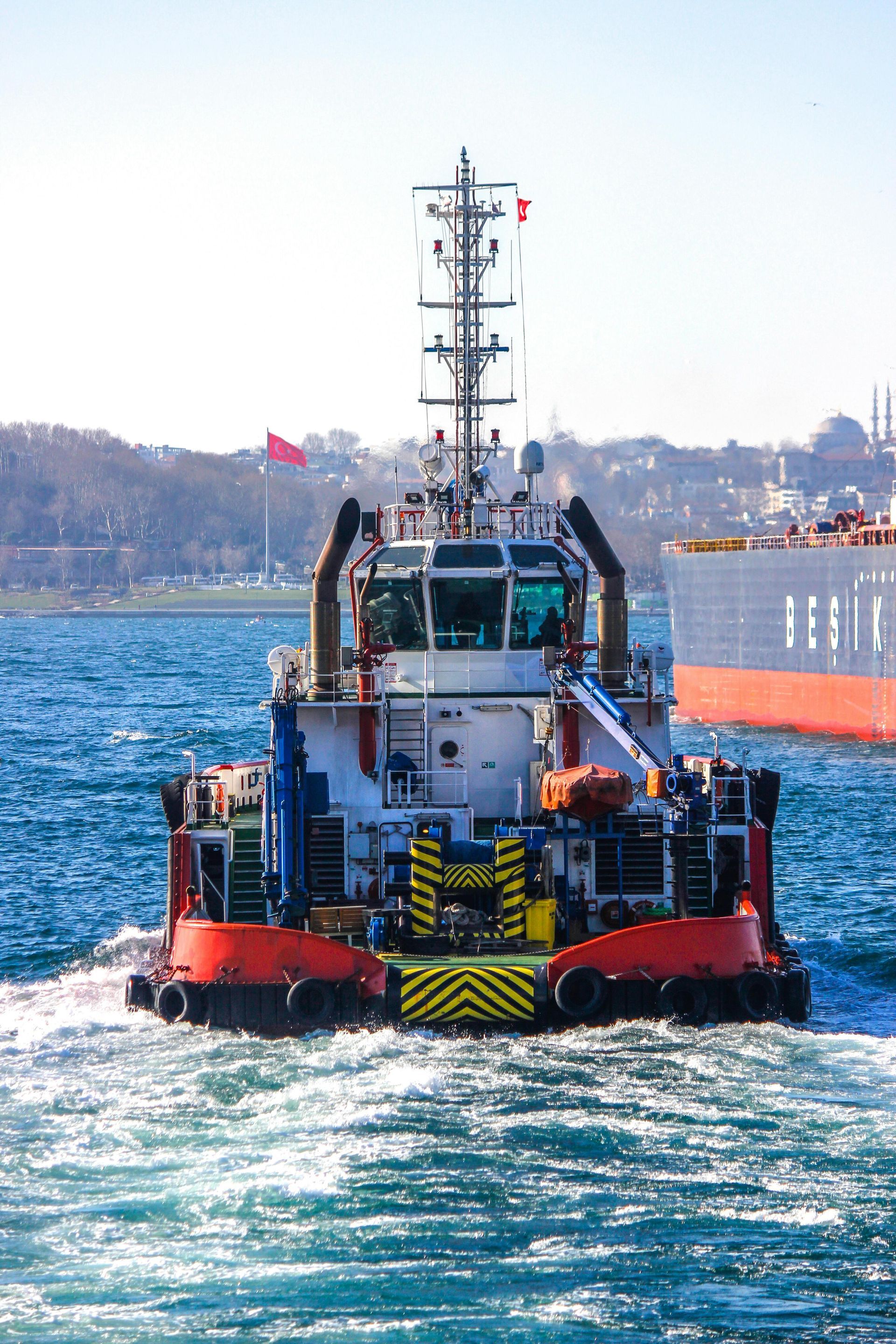 Red and white tugboat on the water with a tall mast, churning water behind it.