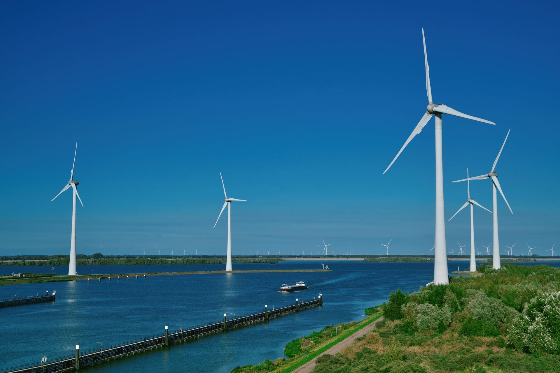 Wind turbines generating electricity in a blue water setting, with a boat and clear sky.