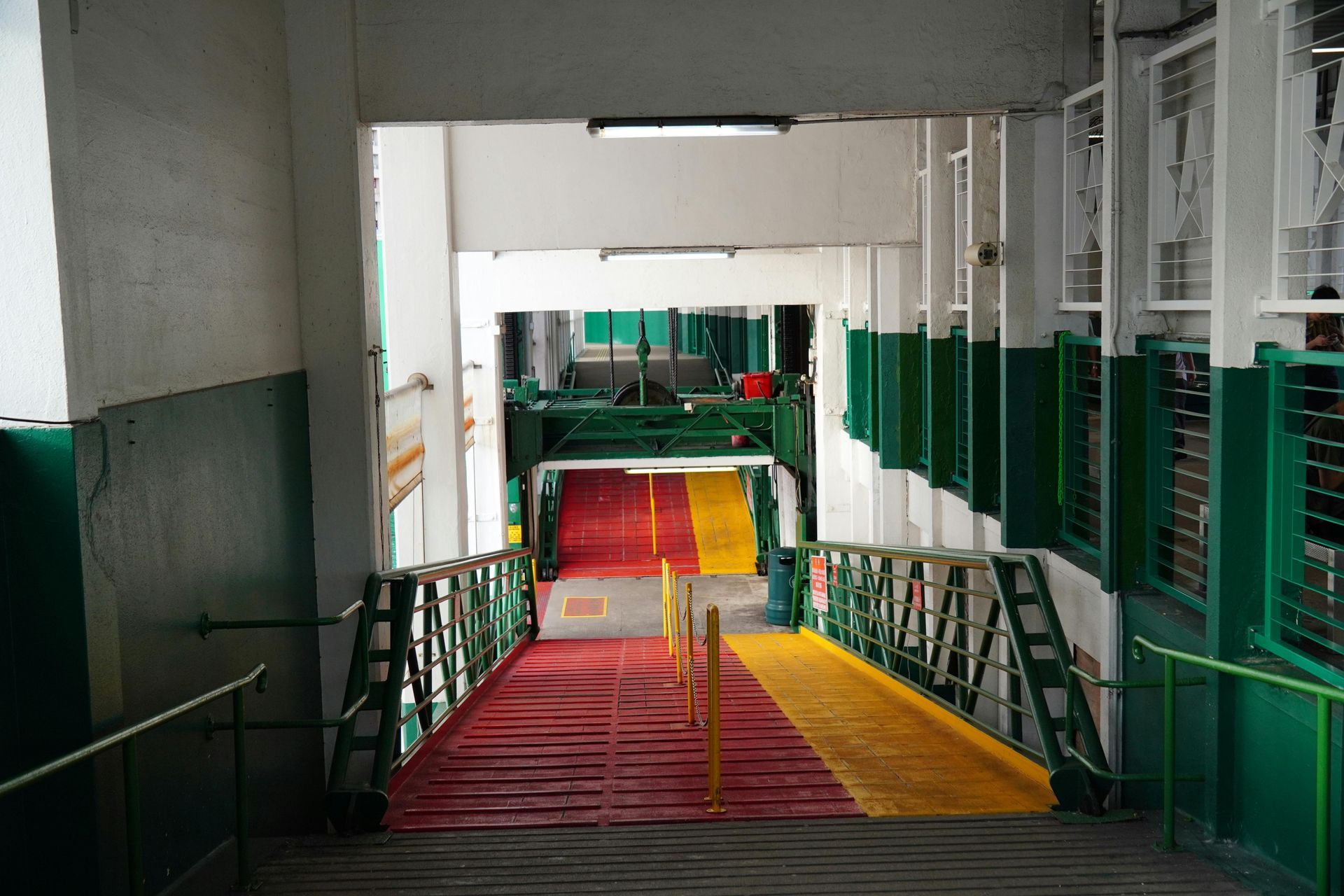 View down a ferry ramp. Red and yellow floor leads to an open deck. Green and white walls.