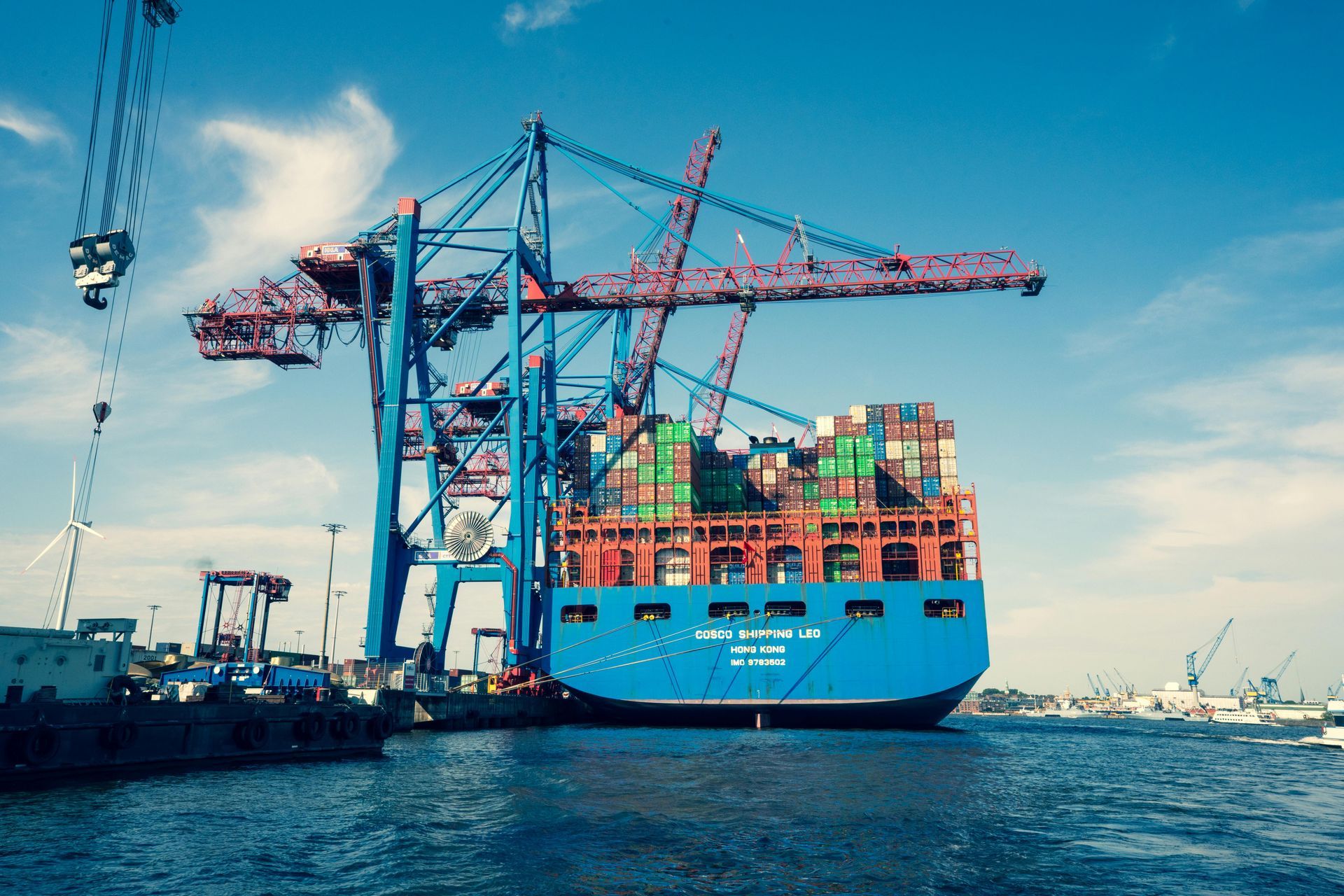 Blue cargo ship being unloaded by large red and blue cranes at a harbor.