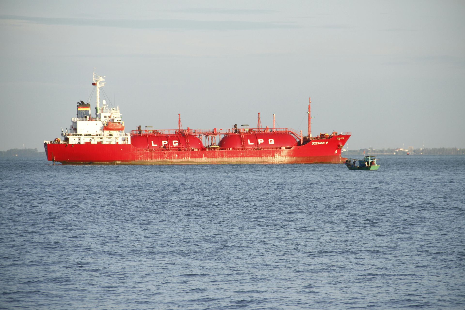 Red tanker ship on blue water with a small boat nearby.