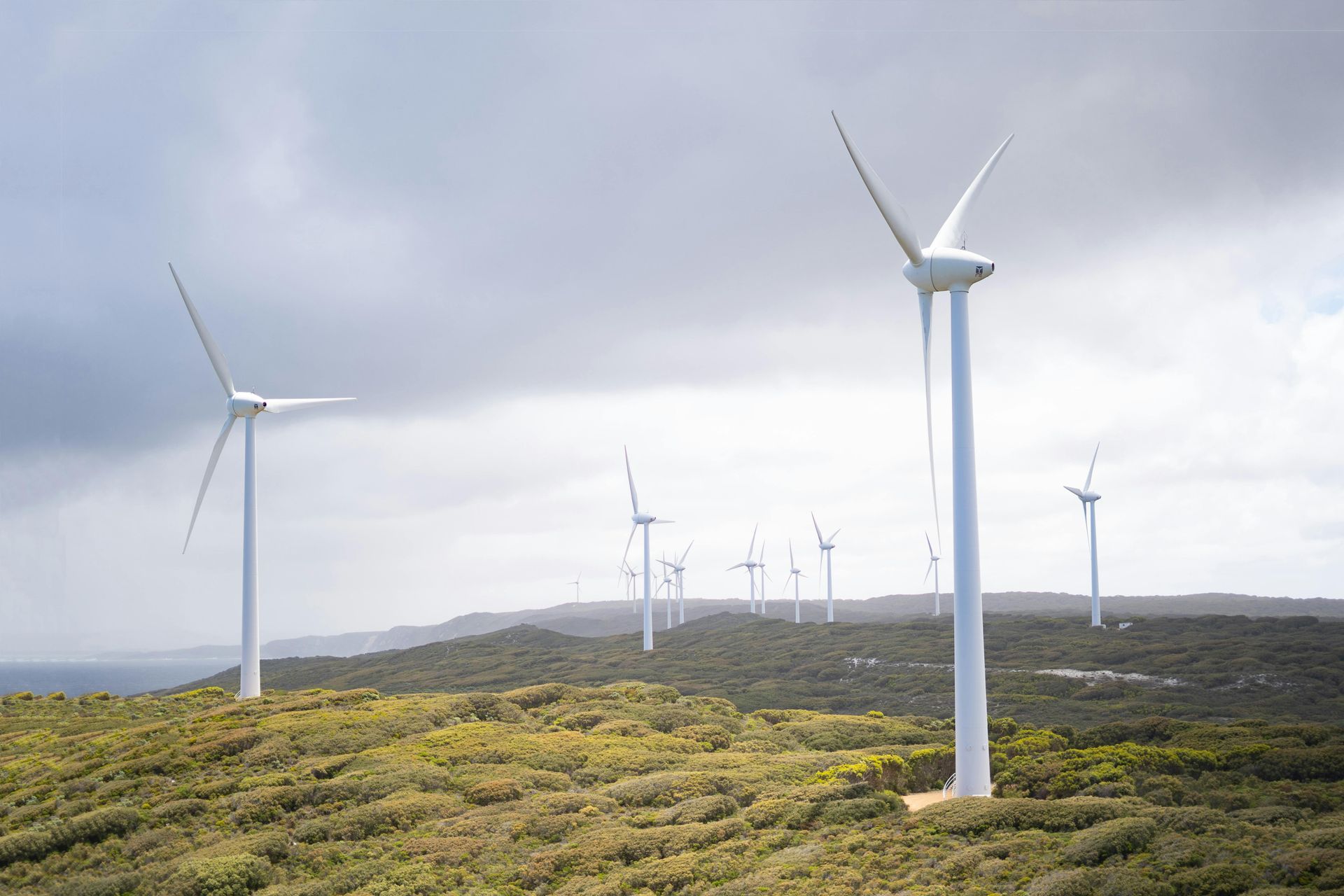 Wind turbines on a hilltop, generating clean energy under a cloudy sky.
