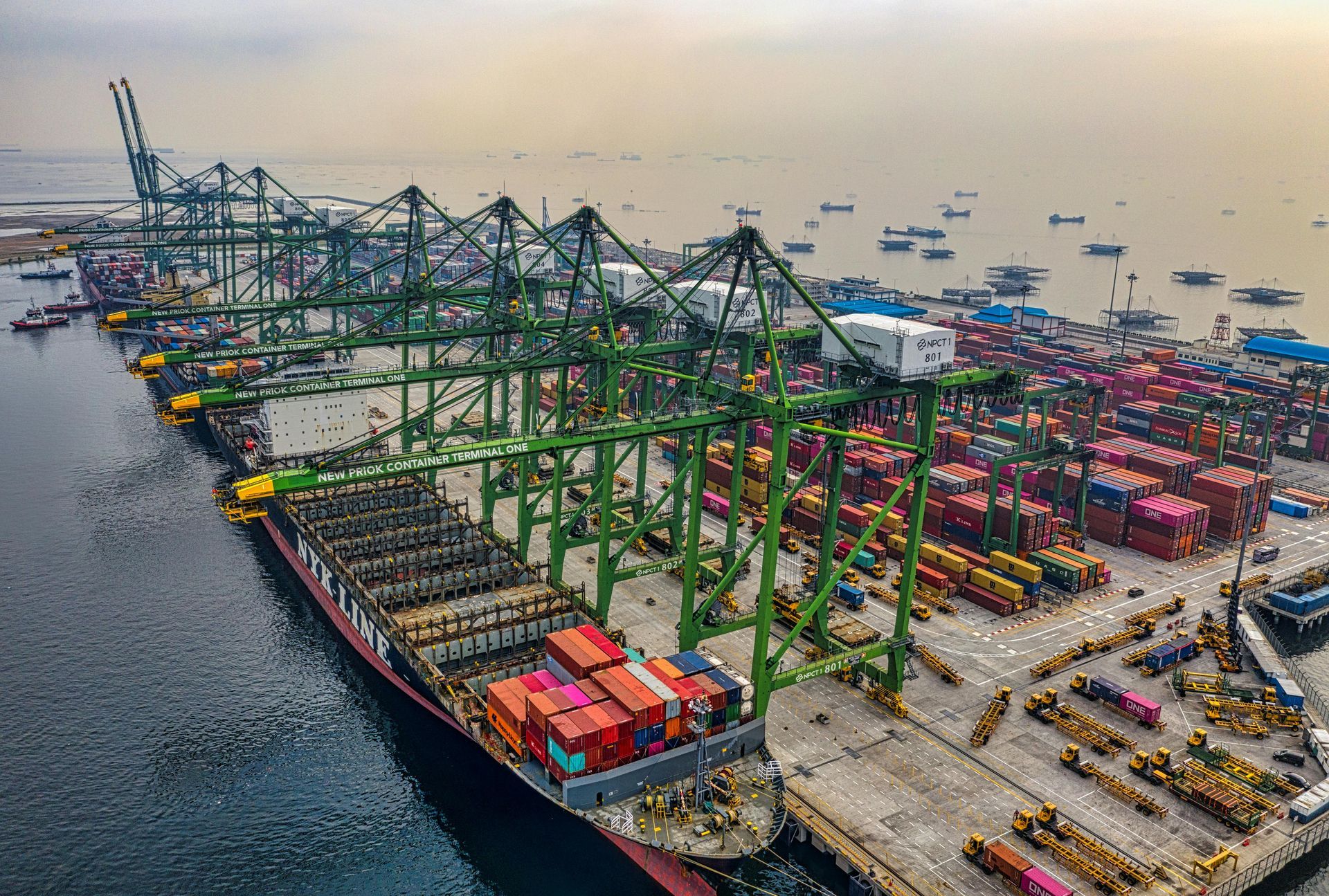 Aerial view of a bustling port with cranes loading cargo onto a large ship, surrounded by containers and water.