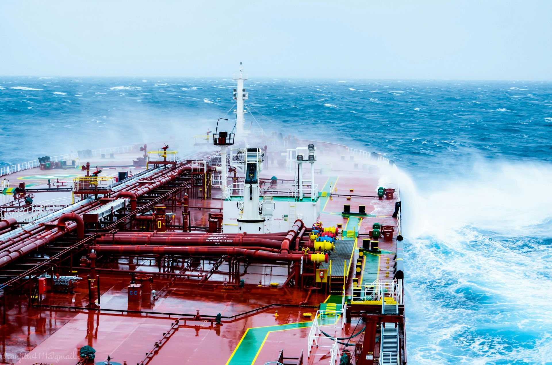 Large cargo ship sailing through rough, stormy ocean, waves crashing over the bow.