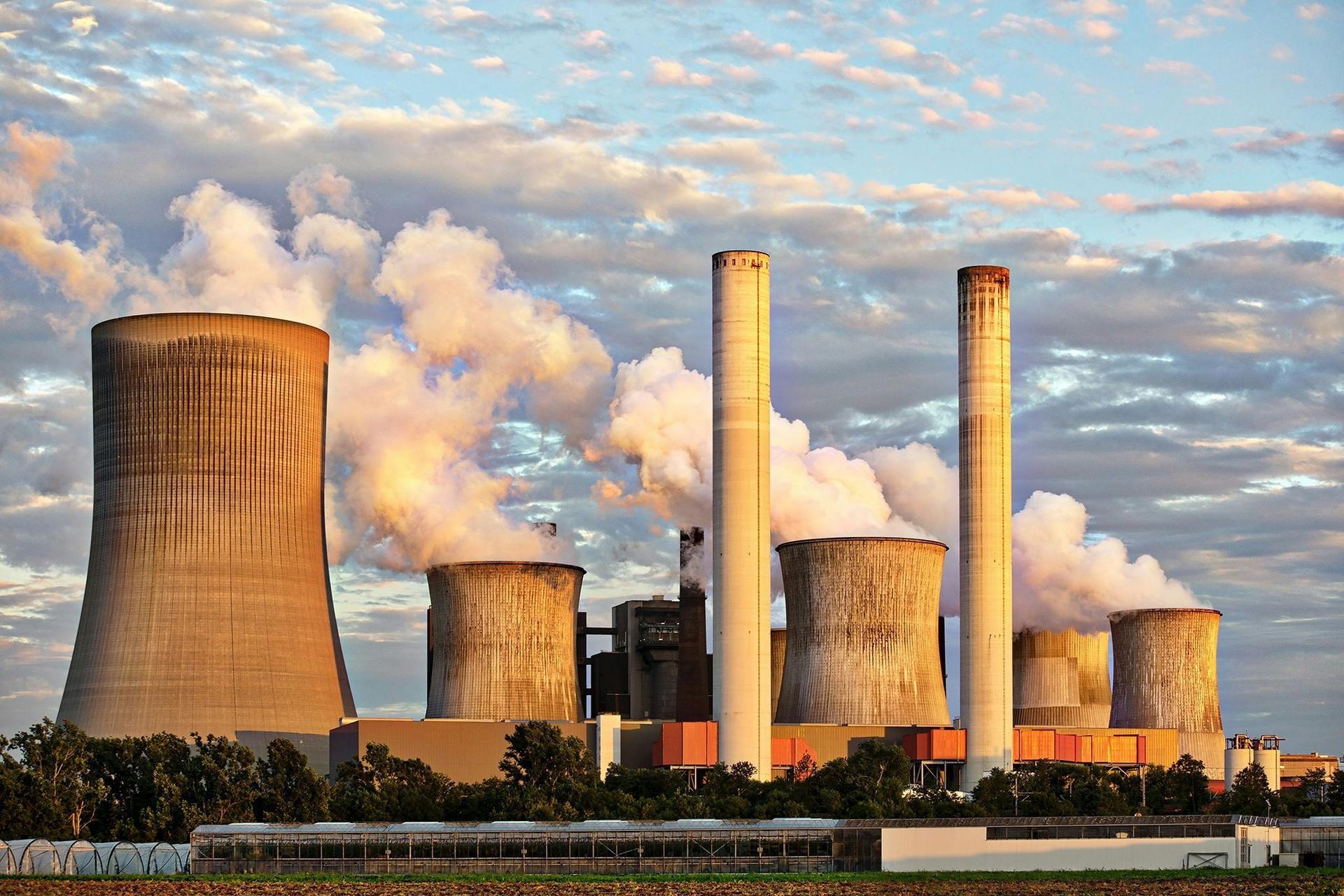 Coal-fired power plant with smoke stacks billowing steam against a cloudy sky.