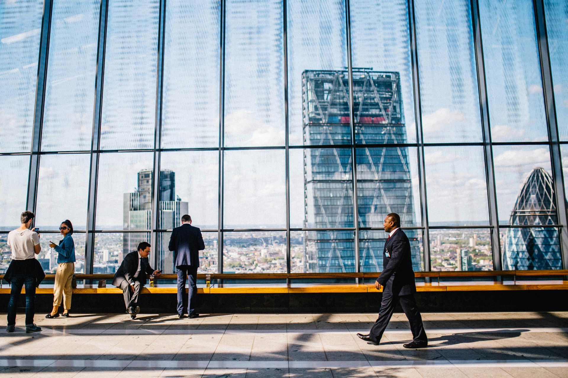 People in suits look out of glass windows at a cityscape.