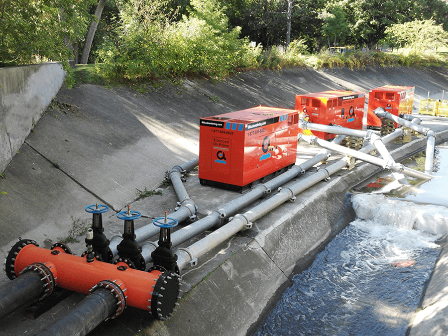 Pompes et tuyaux rouges dans un canal de drainage en béton ; l'eau coule.