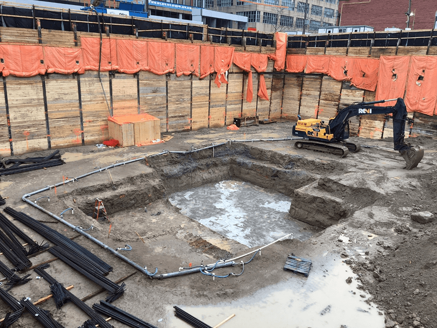 Excavation site with three yellow construction vehicles, wooden walls, and a worker.