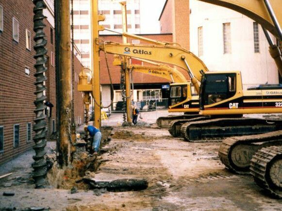 Construction site with yellow excavators and workers alongside a building.