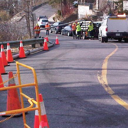 Road construction site with workers, cones, vehicles, and equipment; sunny day.