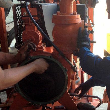 Deux personnes travaillant sur une machine orange, peut-être une pompe.