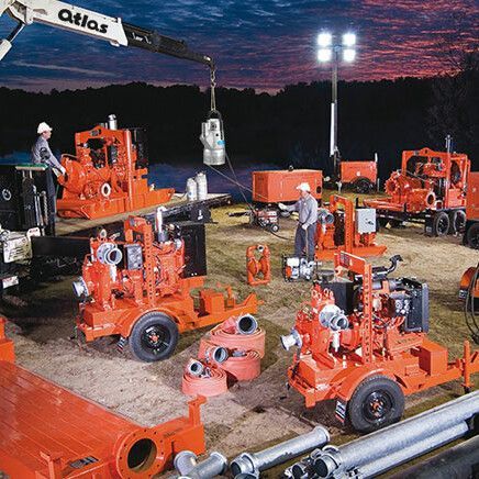 Des ouvriers assemblent des pompes industrielles orange la nuit, éclairées par des projecteurs.