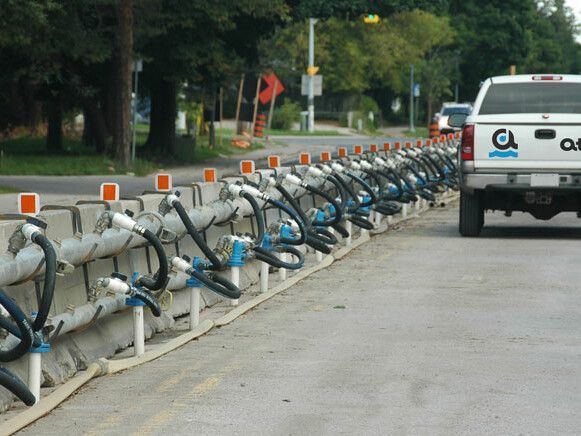 A line of connected water-filled barriers along a road. A white truck is parked beside them.