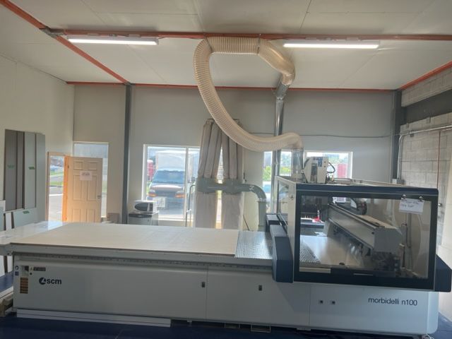 Grande machine CNC dans une usine, avec une table blanche et un bras d'extraction.