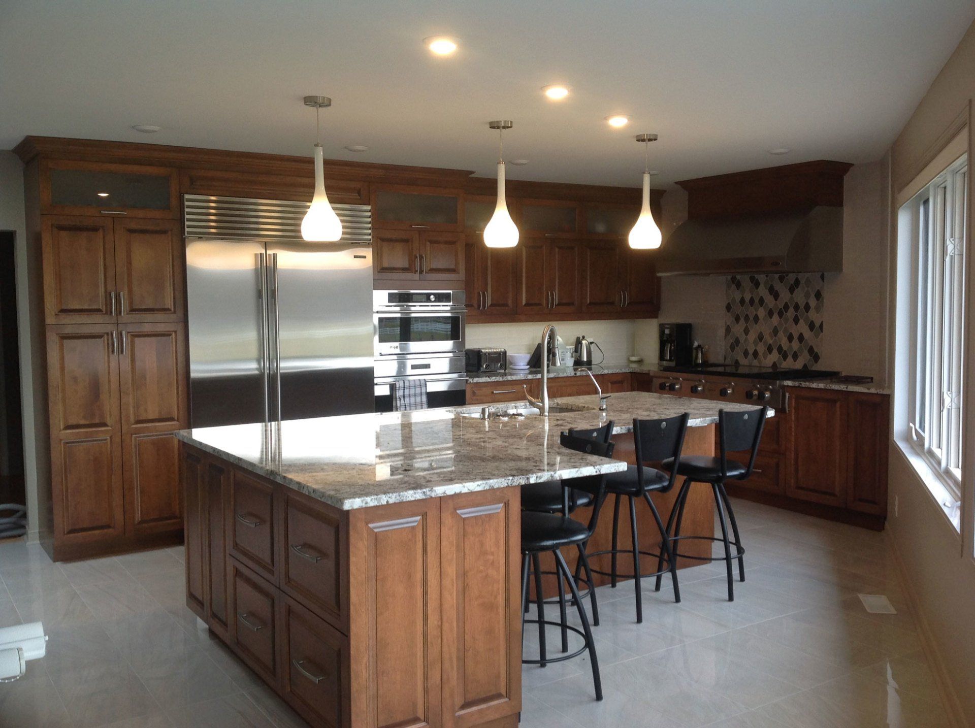 Cuisine spacieuse avec armoires en bois, électroménagers en acier inoxydable, îlot en granit et luminaires suspendus.