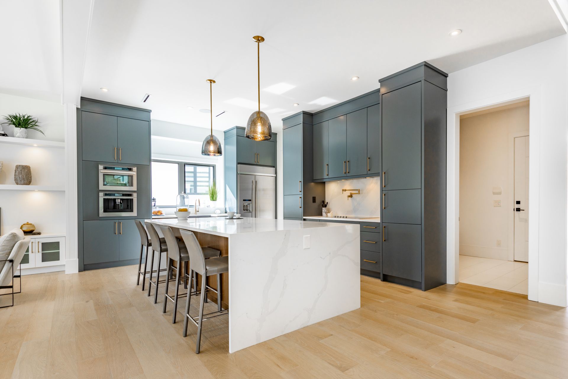 Cuisine moderne avec armoires grises, îlot blanc, luminaires suspendus dorés et planchers de bois franc.