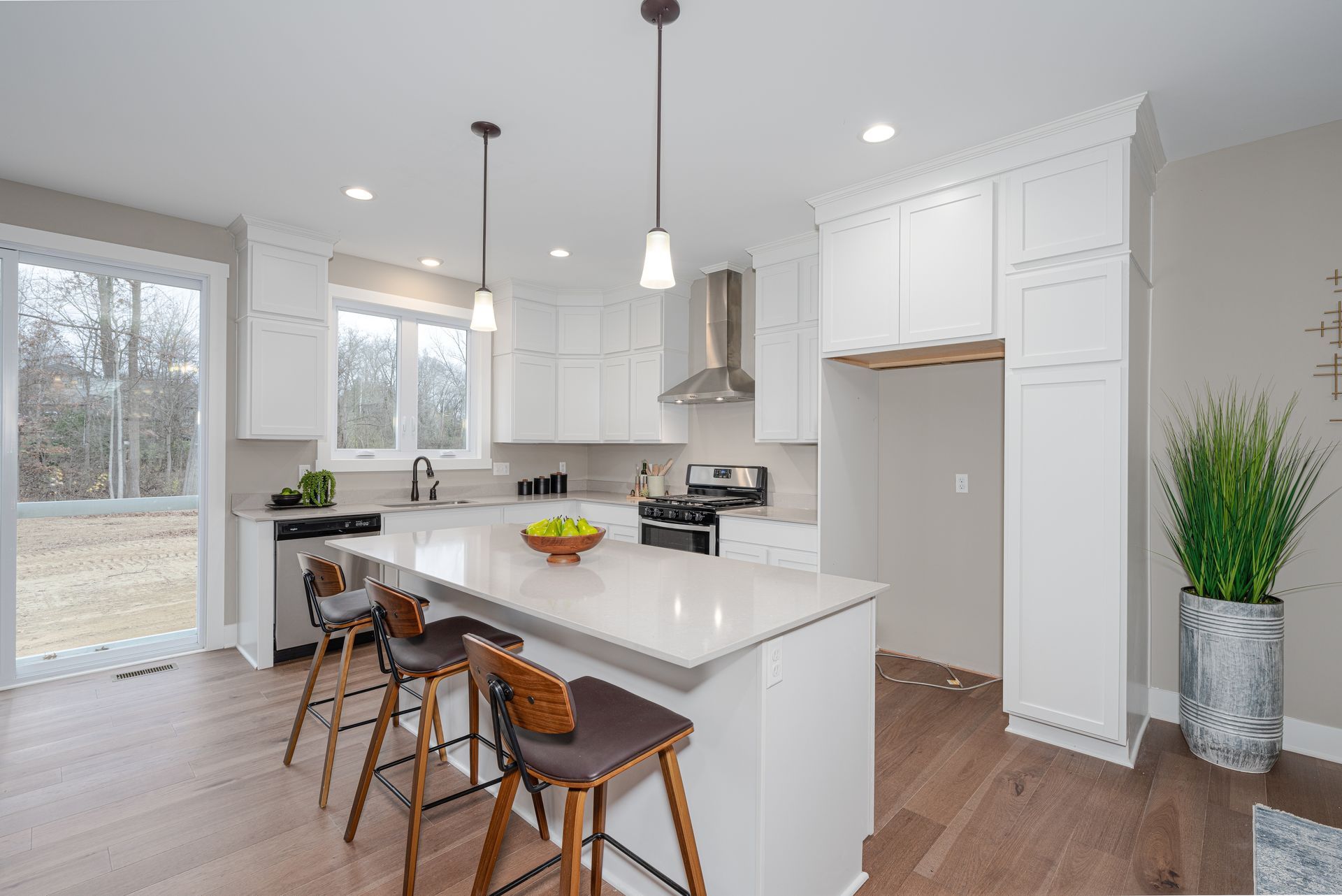 Cuisine blanche moderne avec îlot, planchers de bois, électroménagers en acier inoxydable et tabourets de bar.