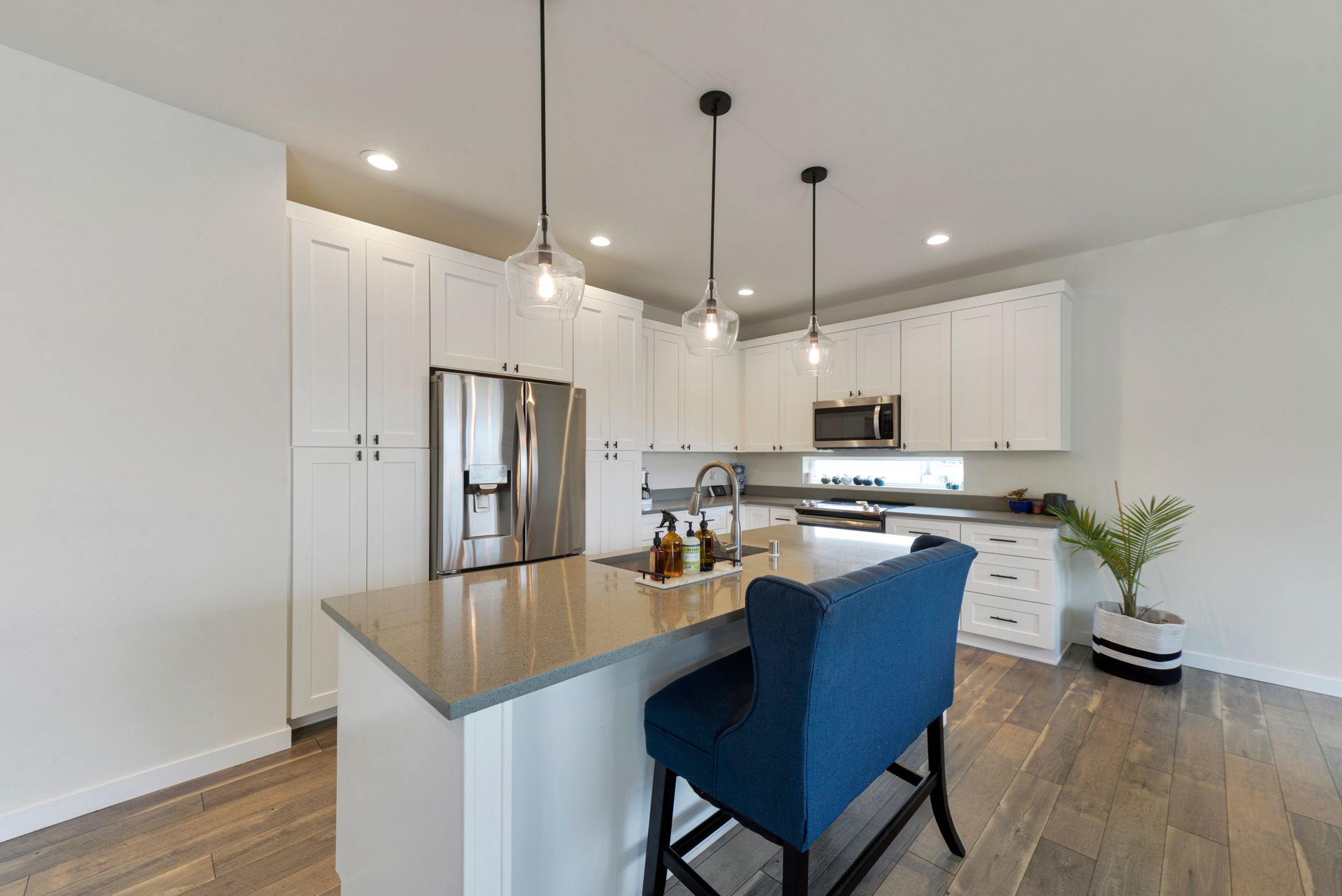 Cuisine blanche moderne avec îlot, électroménagers en acier inoxydable, chaise bleue et planchers de bois.