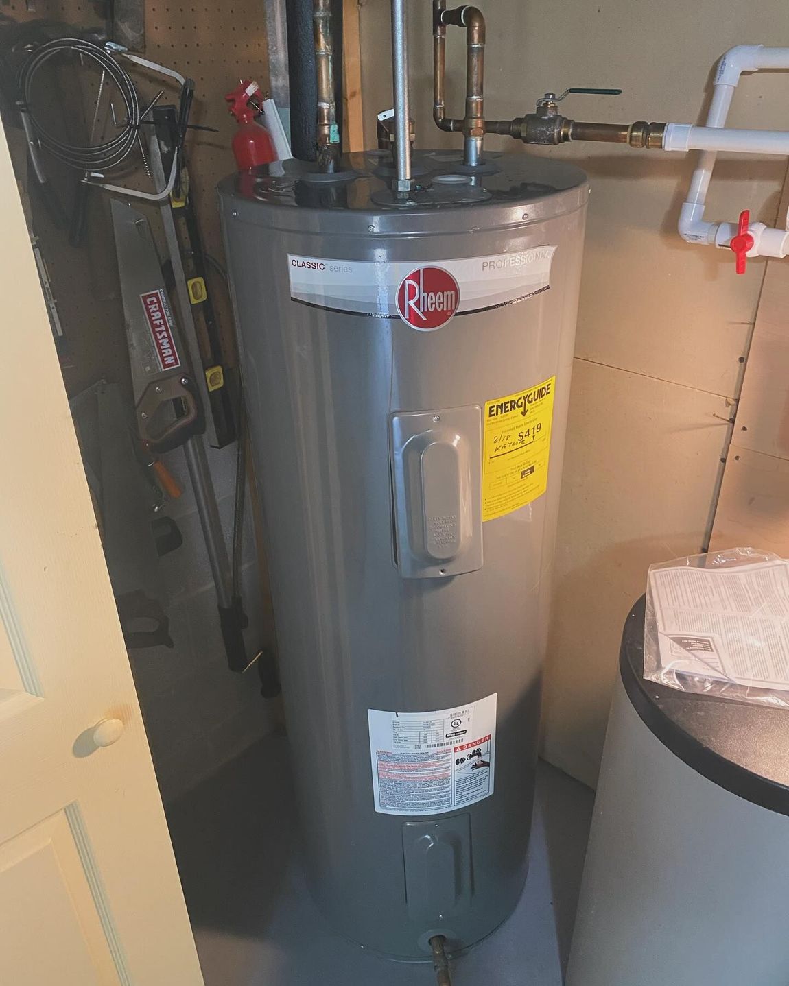 A gray water heater is sitting in a room next to a ladder.