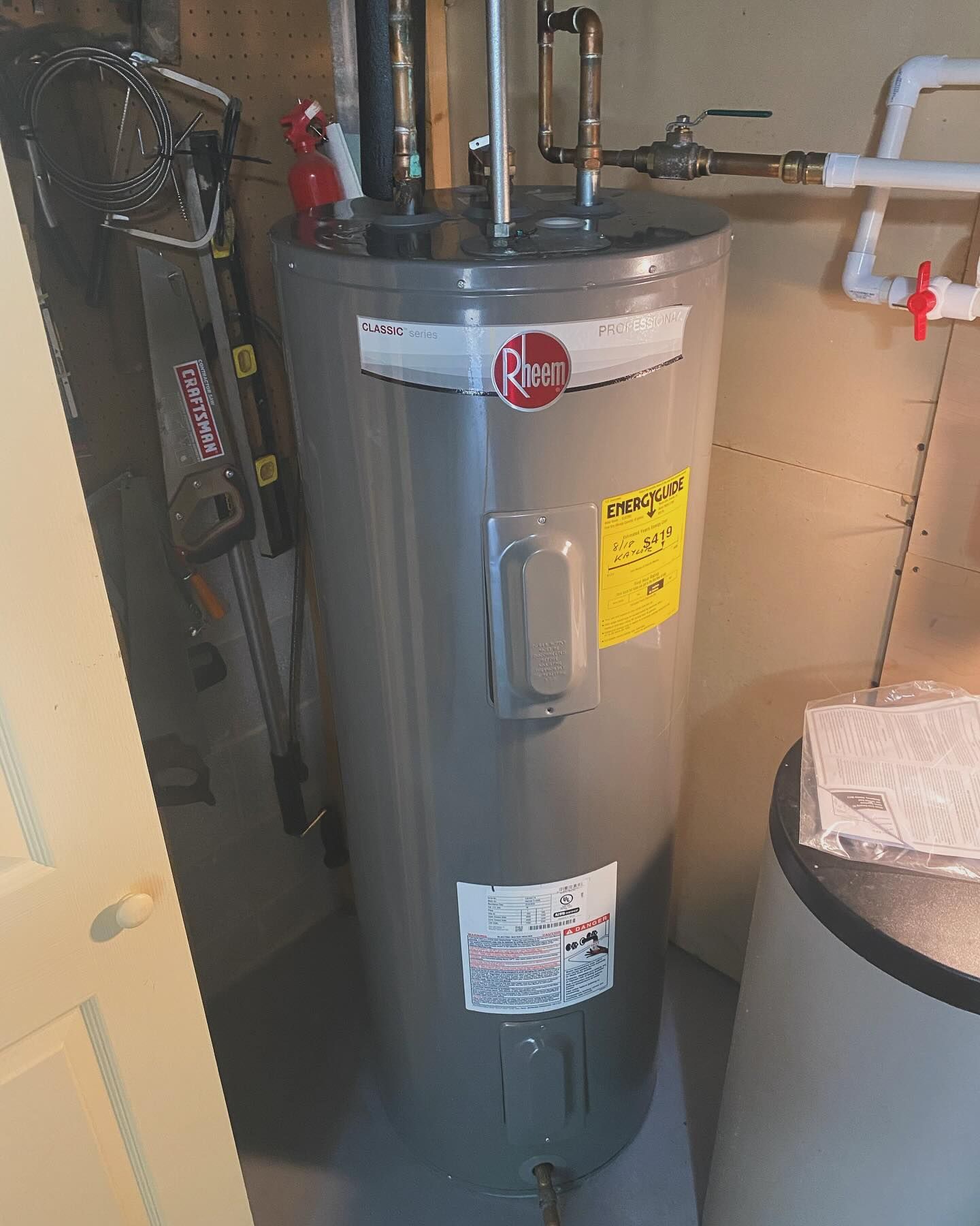 A gray water heater is sitting in a room next to a ladder.