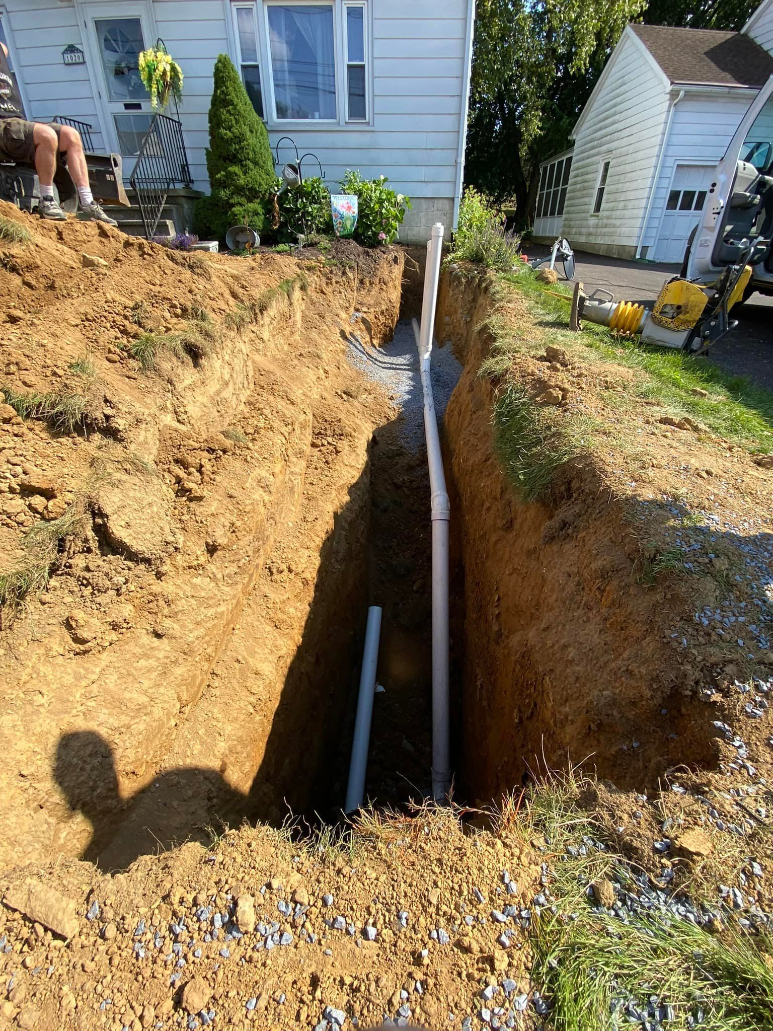 A pipe is being installed in a trench in front of a house.