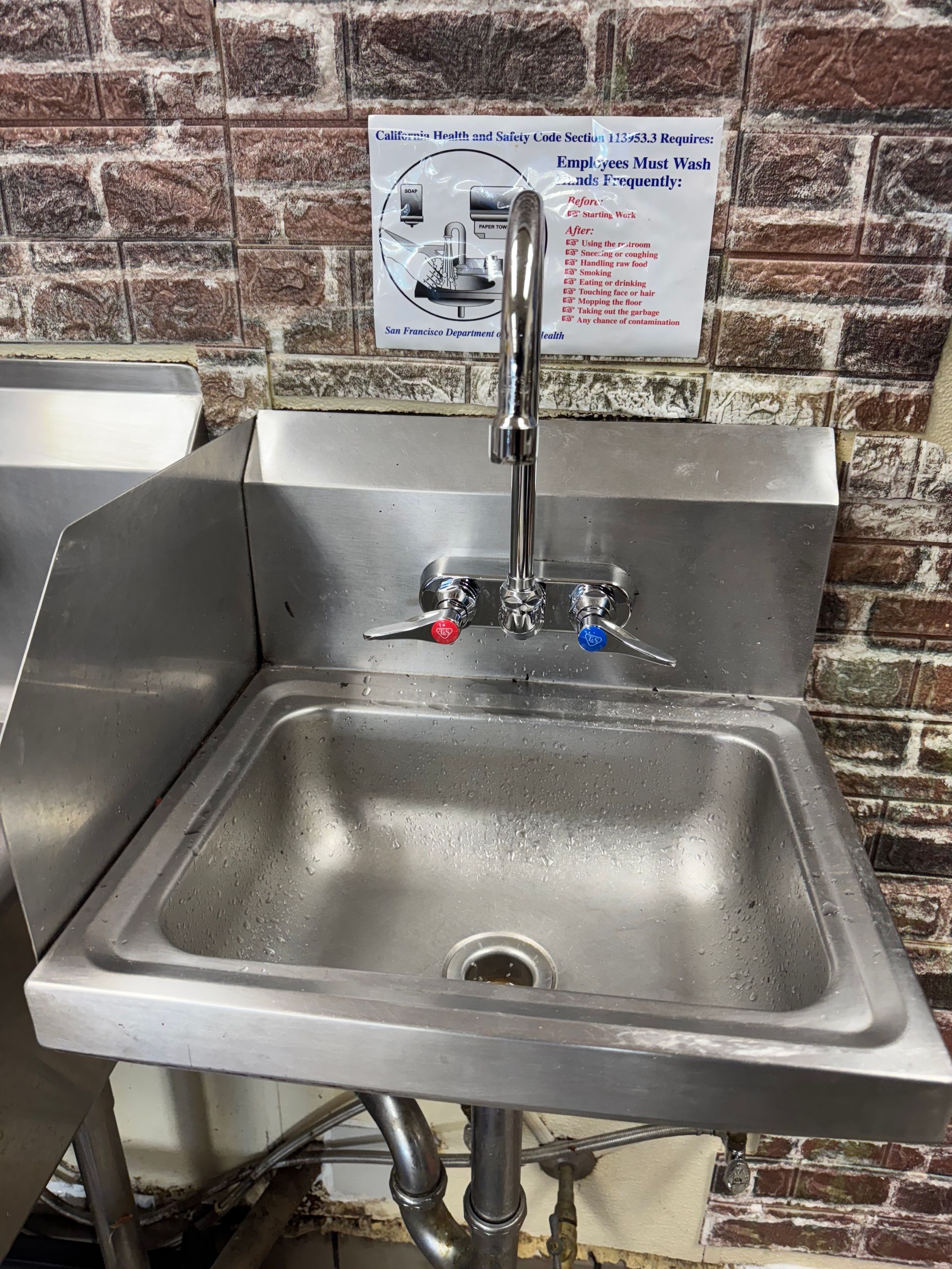 A stainless steel sink with a faucet on a brick wall.