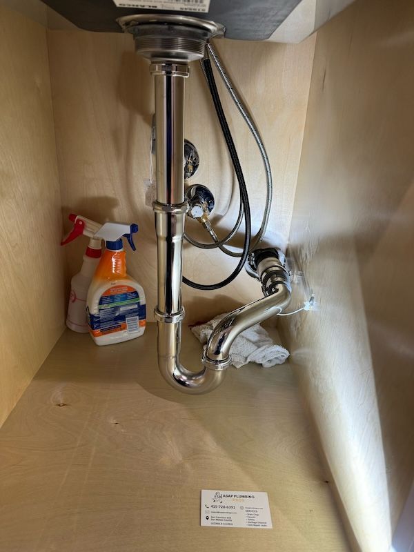 A sink under a cabinet with a spray bottle and a bottle of cleaner.