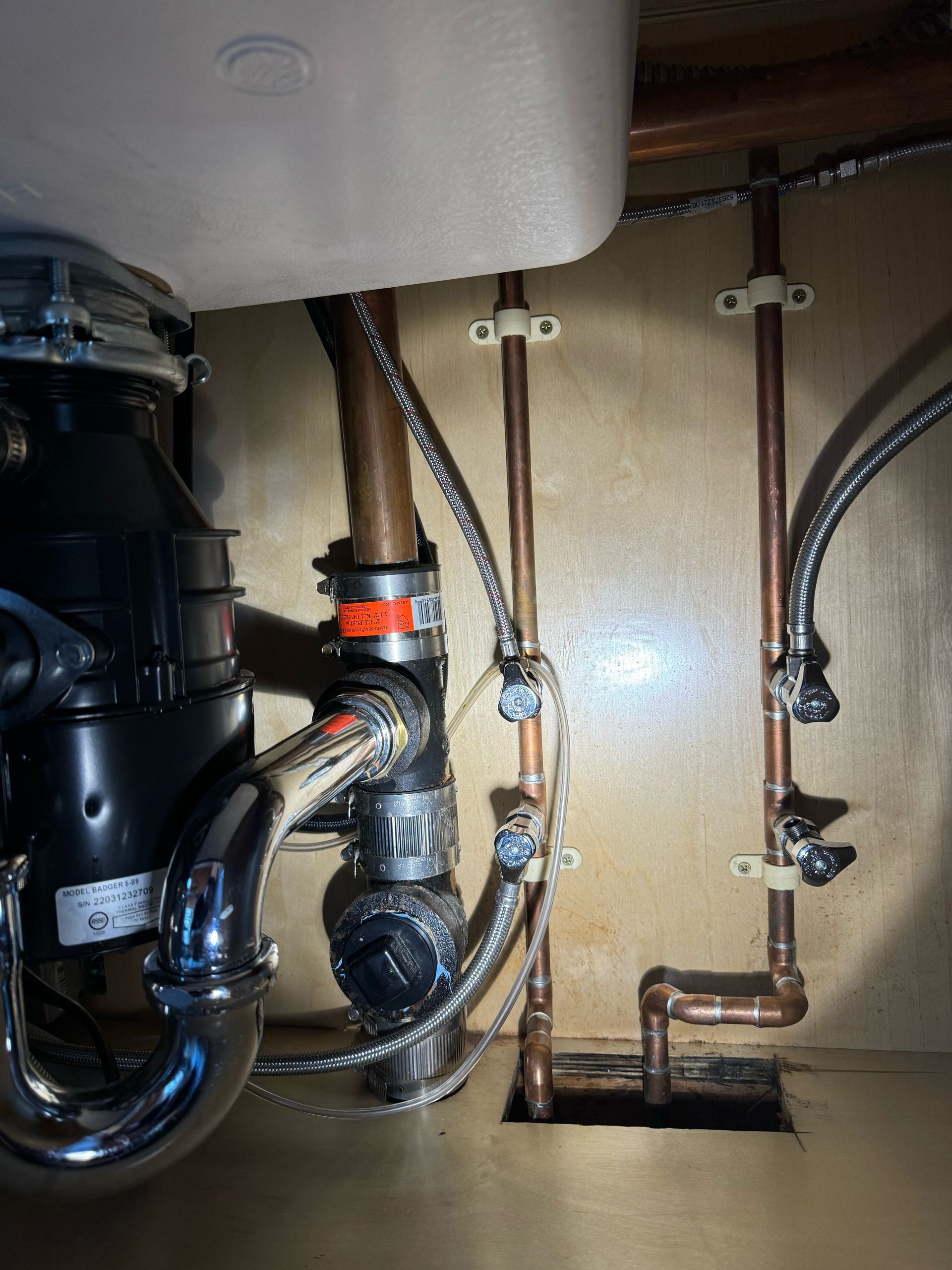 A sink with a garbage disposal and copper pipes underneath it