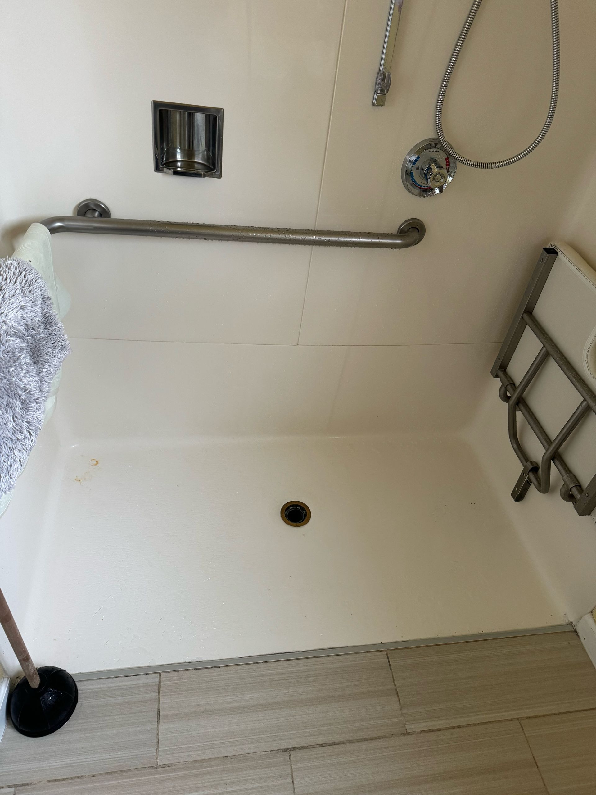 A bathroom with a shower and a plunger on the floor.