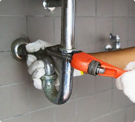 A person is fixing a sink pipe with a wrench.