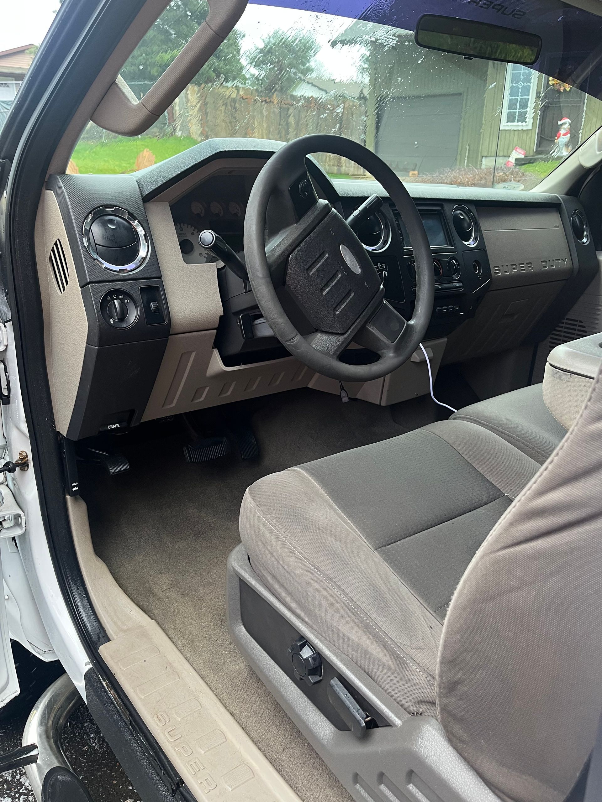 The interior of a vehicle showing a steering wheel, tan and charcoal dashboard, and cloth bucket seats.