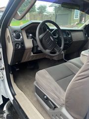 The interior of a vehicle showing a steering wheel, tan and charcoal dashboard, and cloth bucket seats.