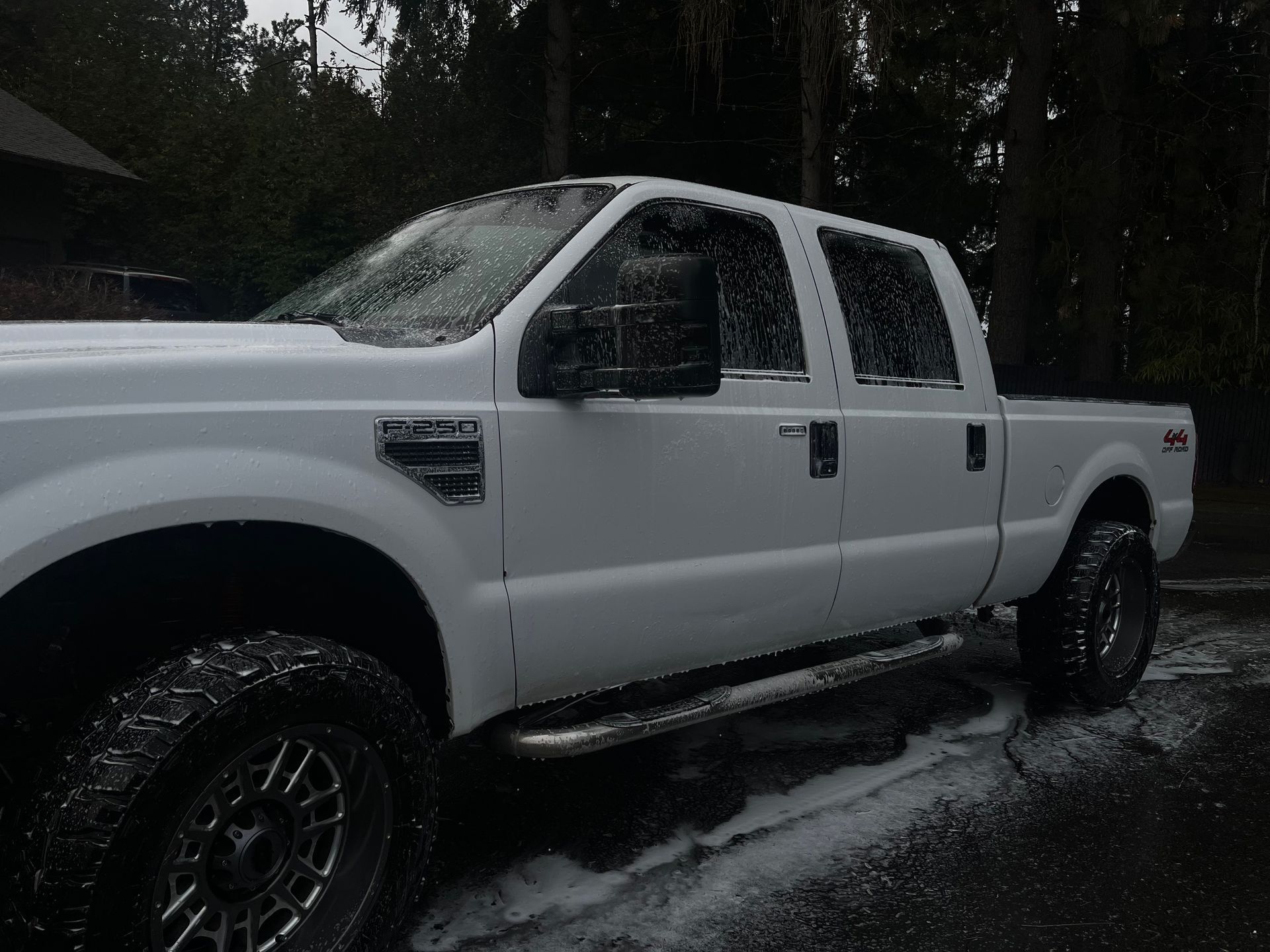 A white Ford Super Duty truck parked outdoors, covered in soap suds during a car wash.