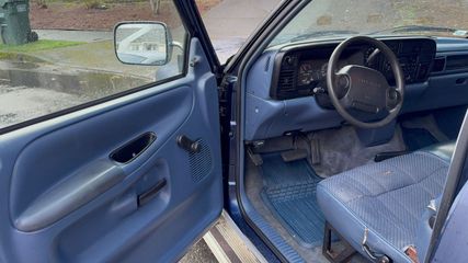 The interior of a vehicle with a blue dashboard, door panel, and cloth seat, viewed through an open driver's door.