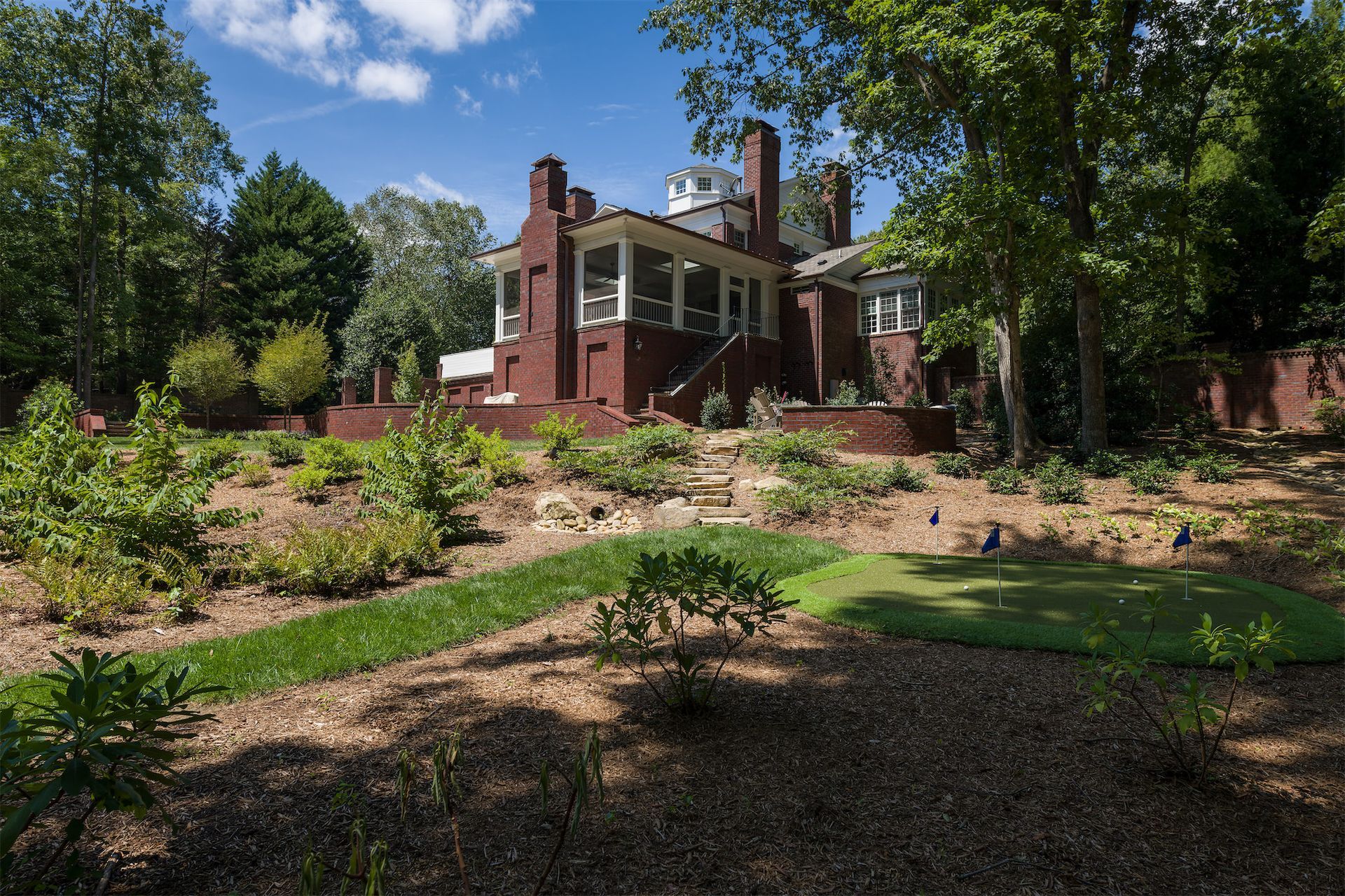 A large brick house with a large porch is surrounded by trees and grass.