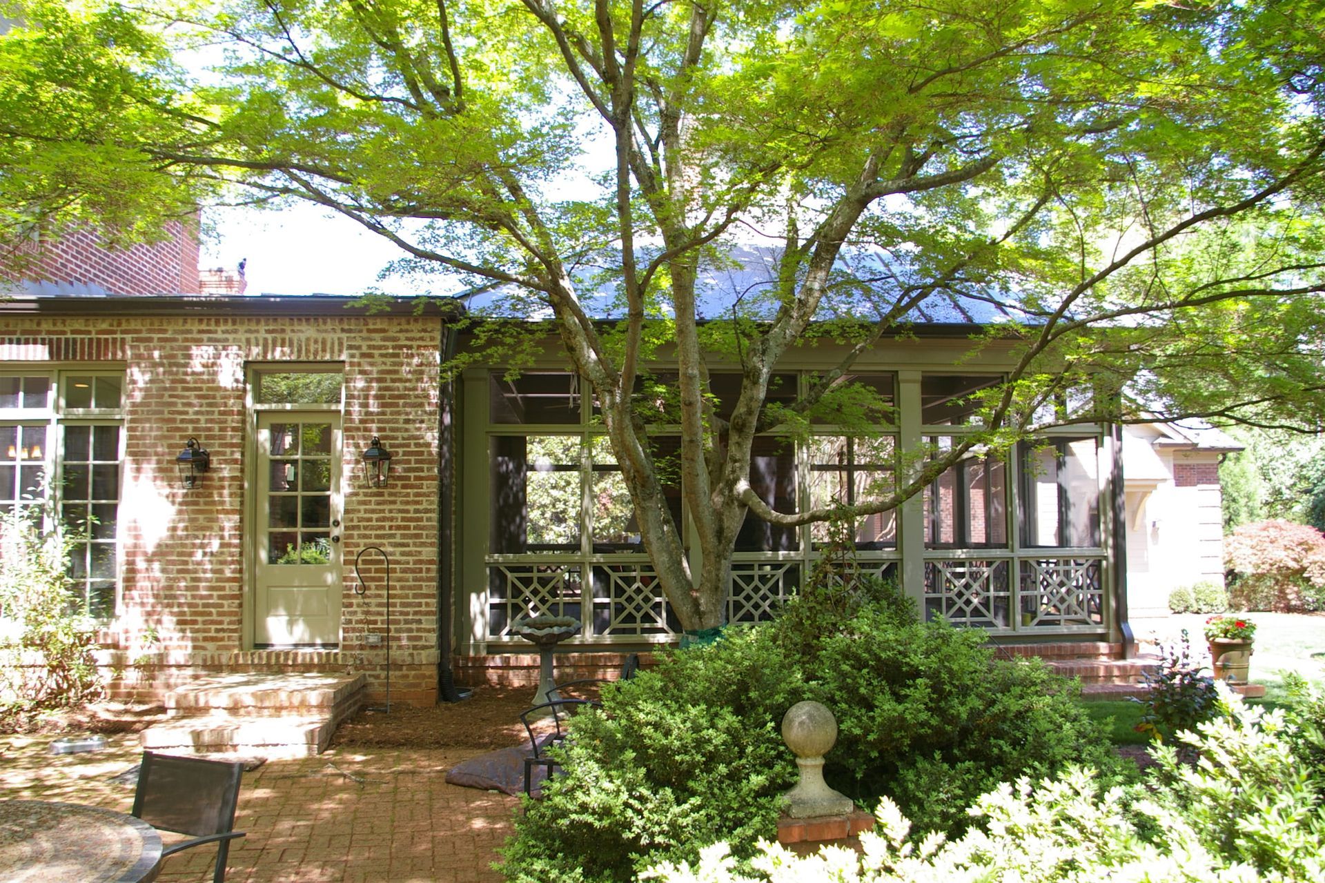 A brick house with a screened in porch and a tree in front of it