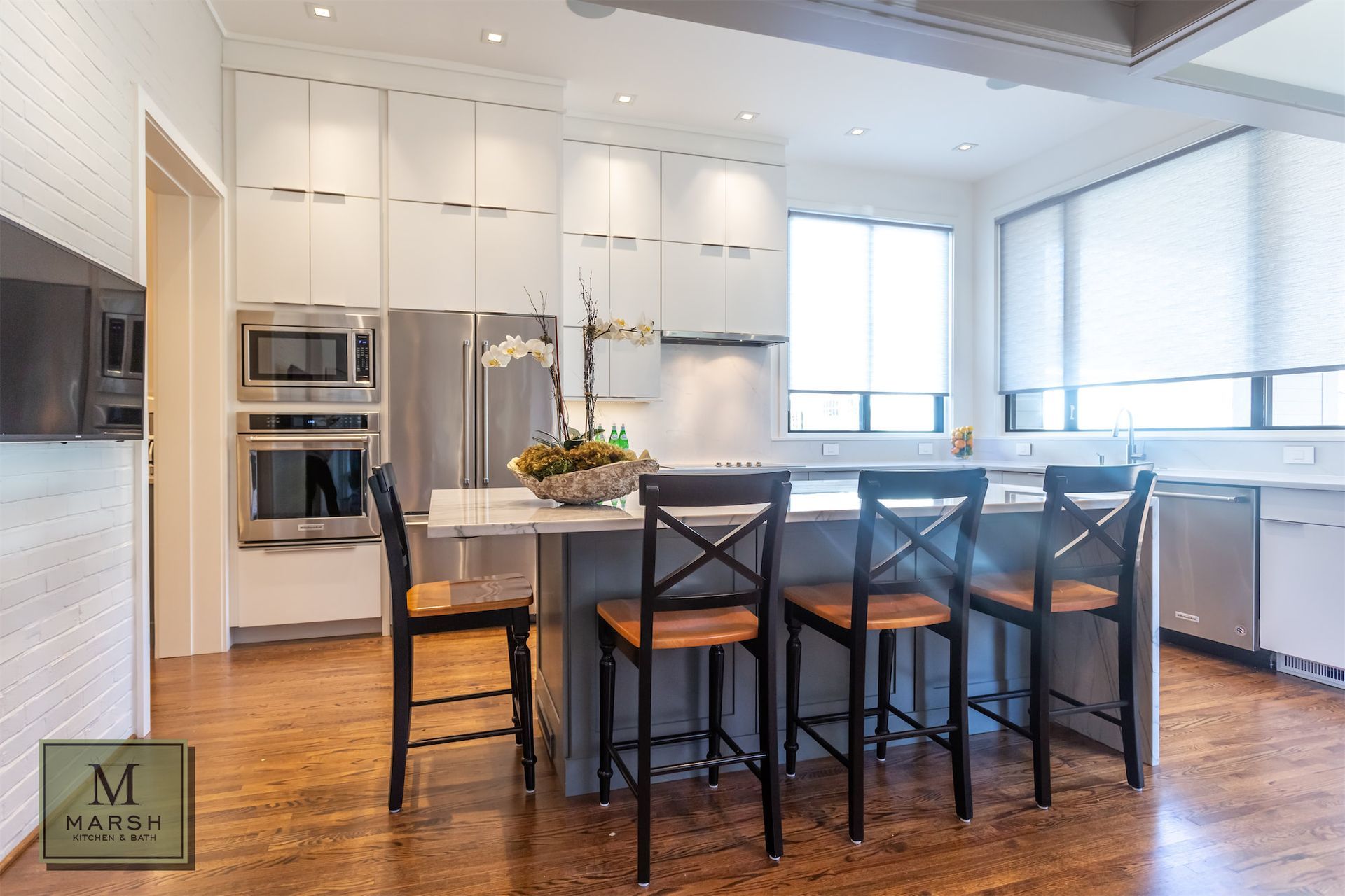 A kitchen with white cabinets , stainless steel appliances , hardwood floors and a large island.