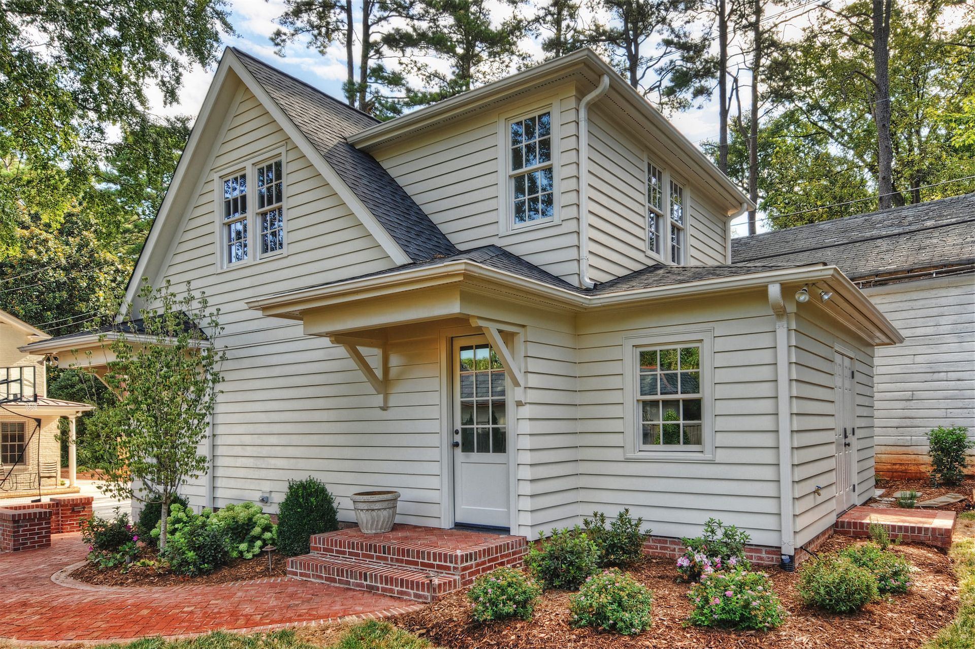 A small white house with a black roof is surrounded by trees.