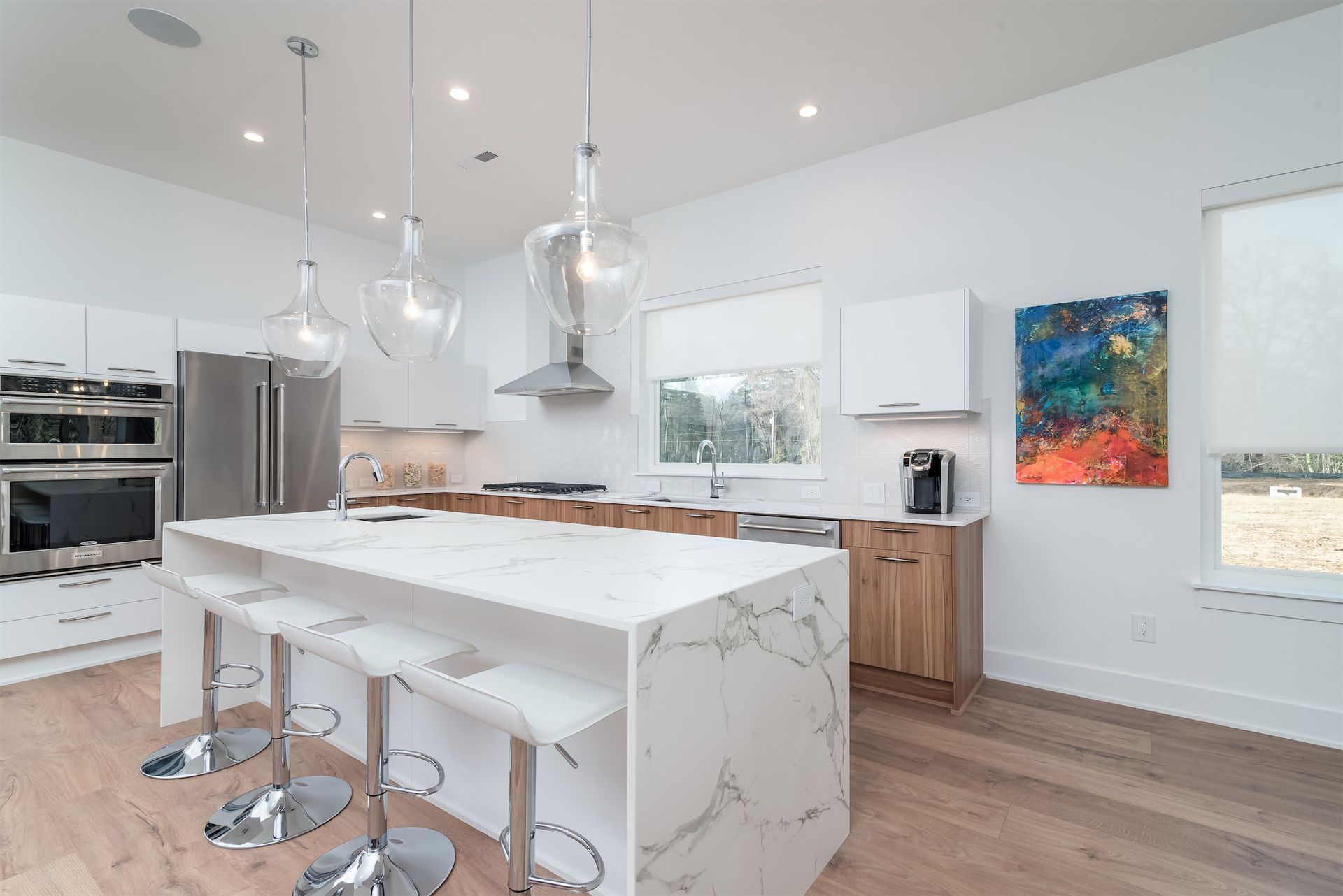 a kitchen with white cabinets , stainless steel appliances , a large island and a painting on the wall .