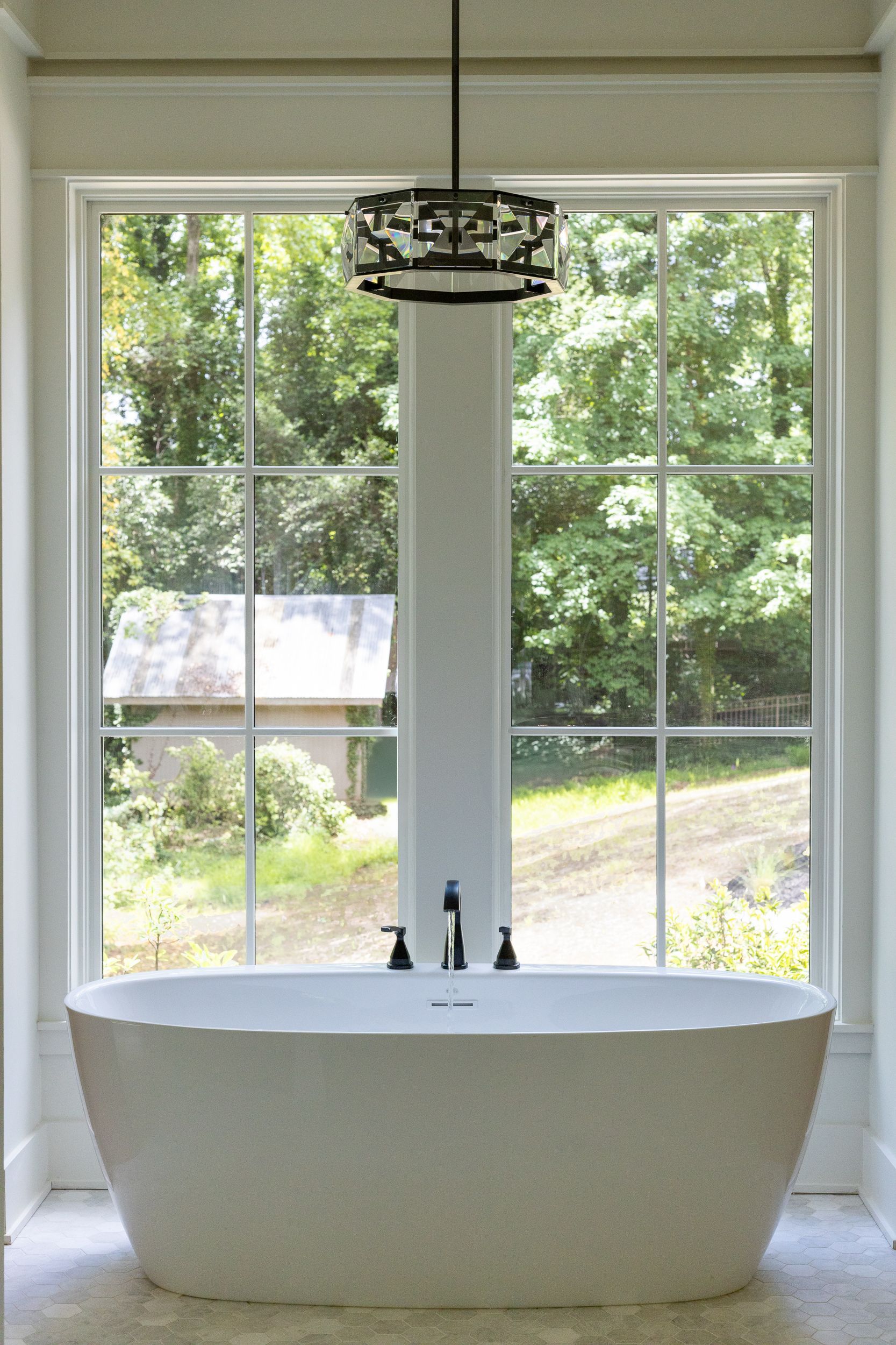 A bathtub is sitting in front of a large window in a bathroom.