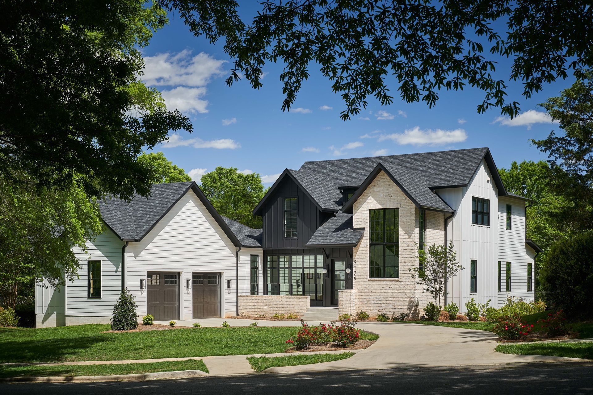 A large white house with a black roof is surrounded by trees.