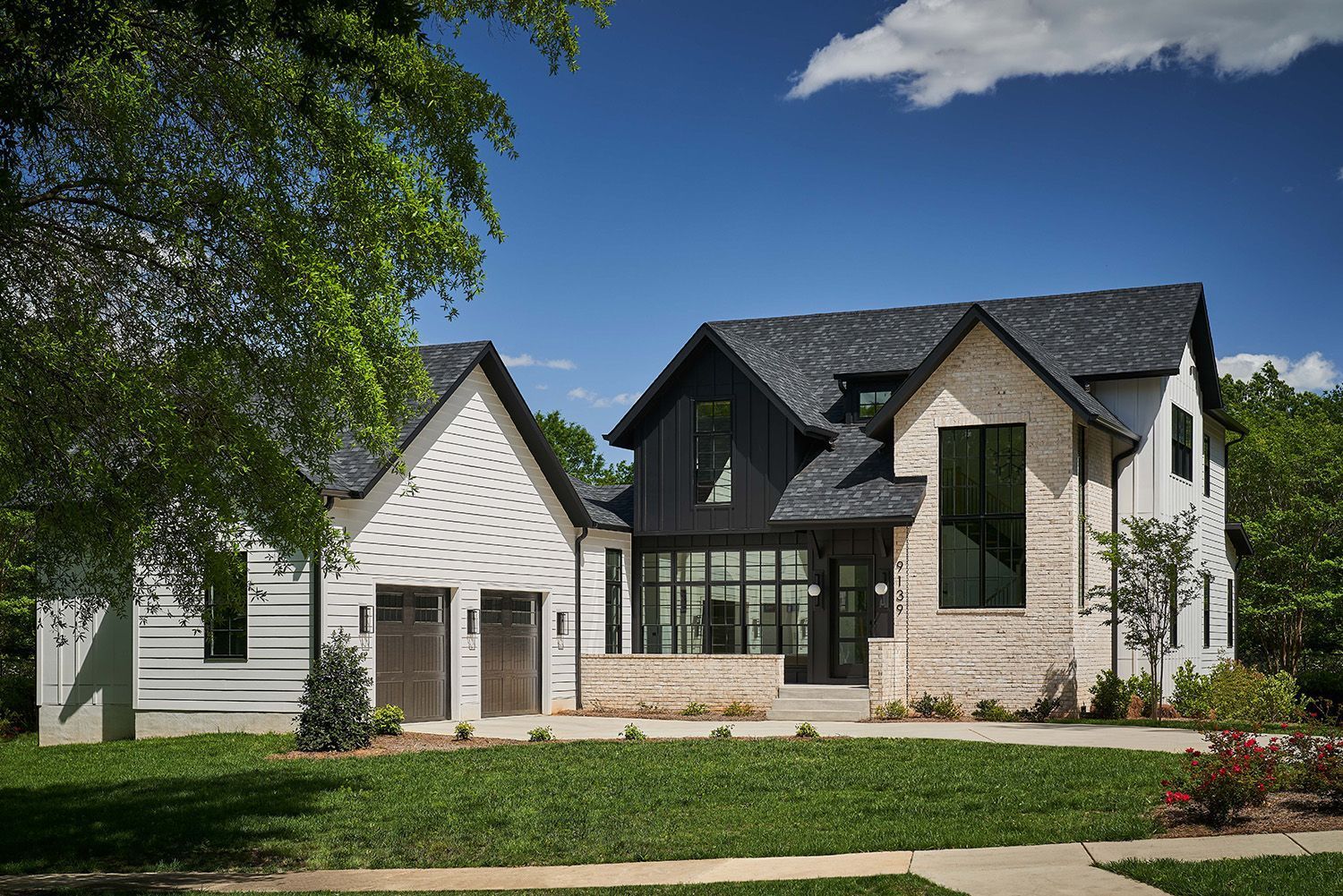 A large white and black house with a black roof is sitting on top of a lush green lawn.