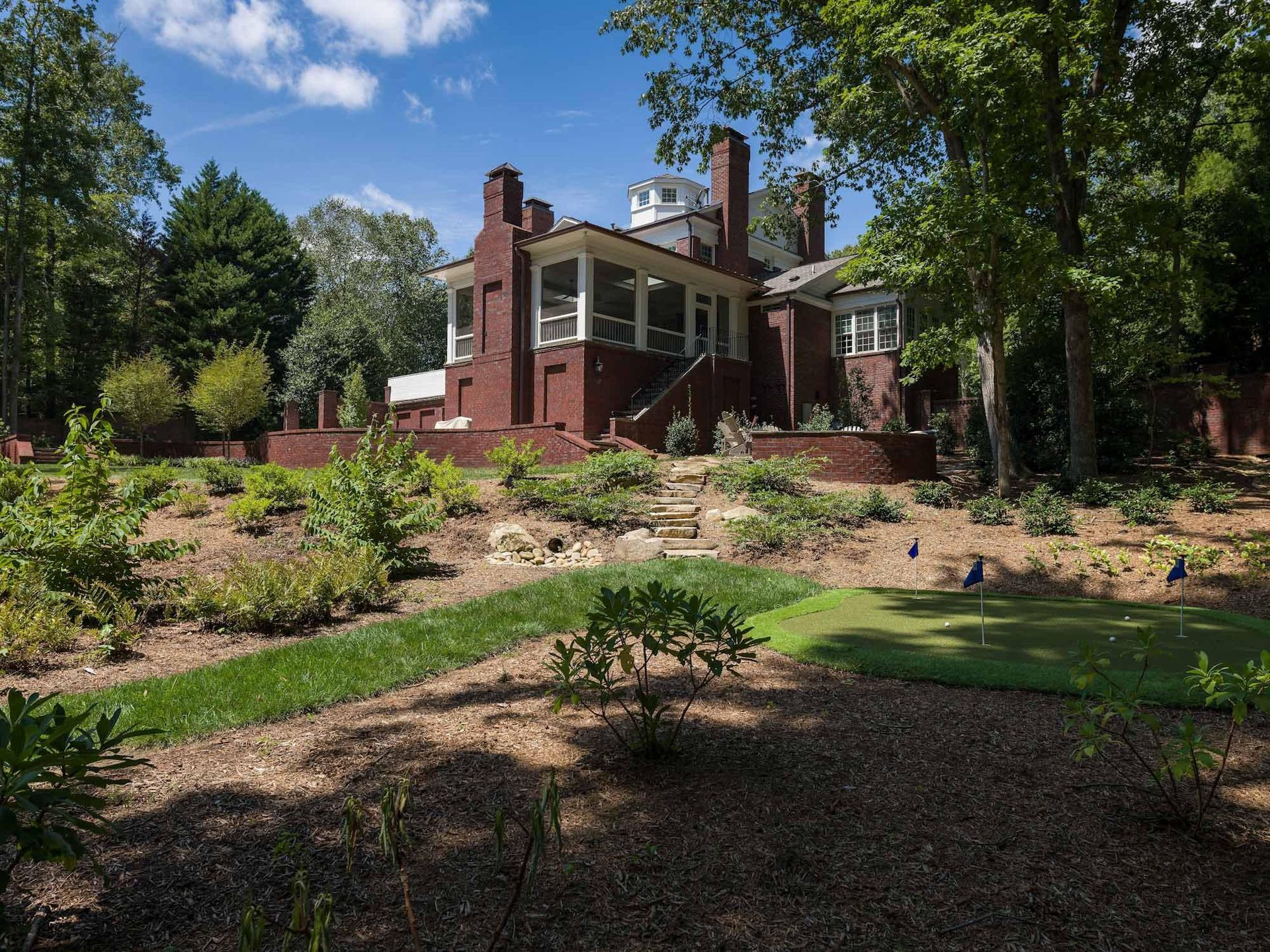 A large brick house sits on top of a hill surrounded by trees.