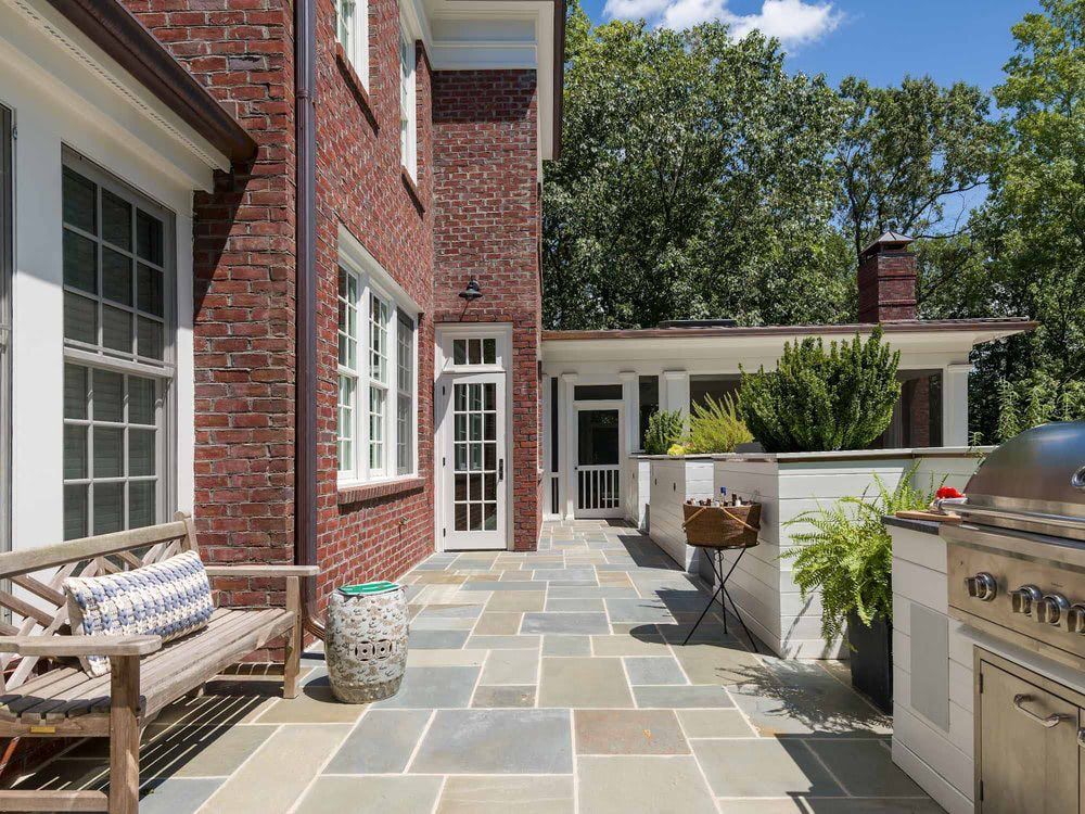 A patio with a grill and a bench in front of a brick house.