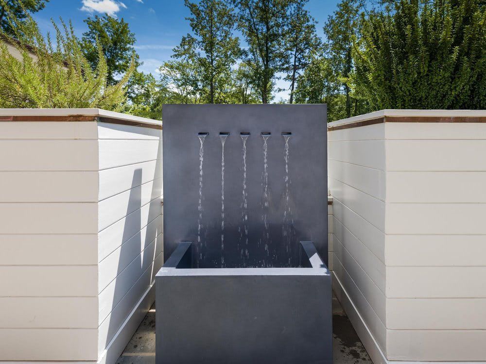 A water fountain is surrounded by white walls and trees