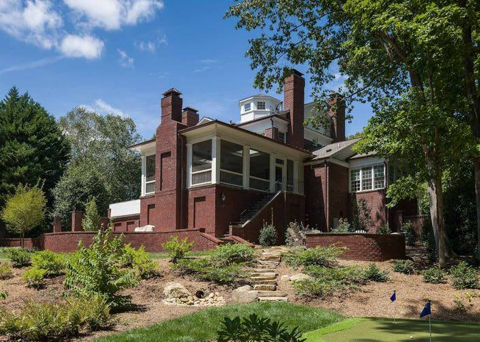 Red brick house with chimney amid trees and landscaped garden under a clear blue sky