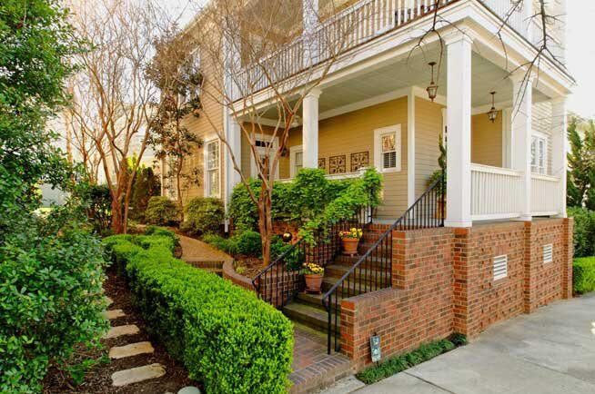 A large house with a porch and stairs is surrounded by trees and bushes.