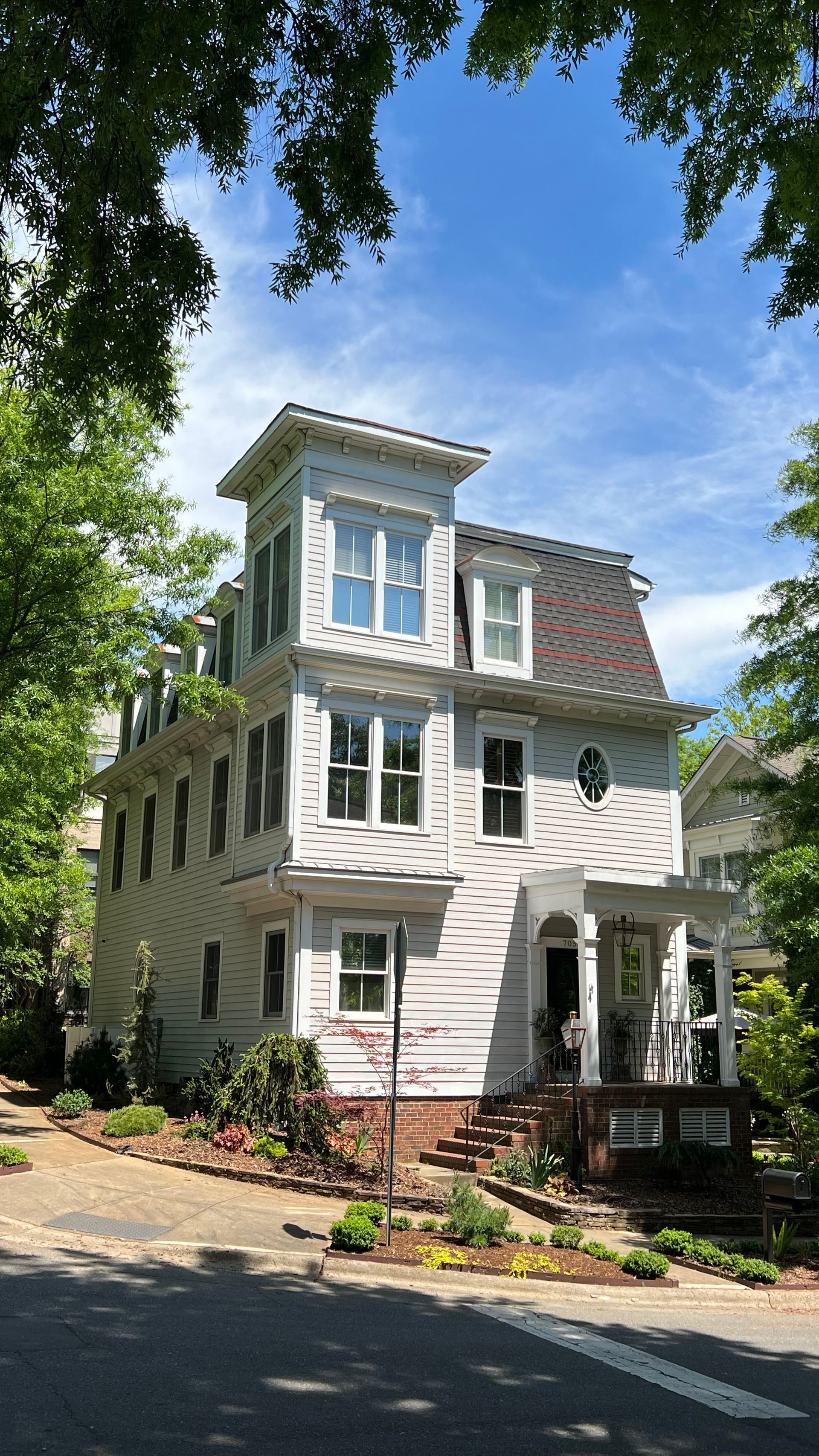 A large white house is sitting on the side of a road surrounded by trees.